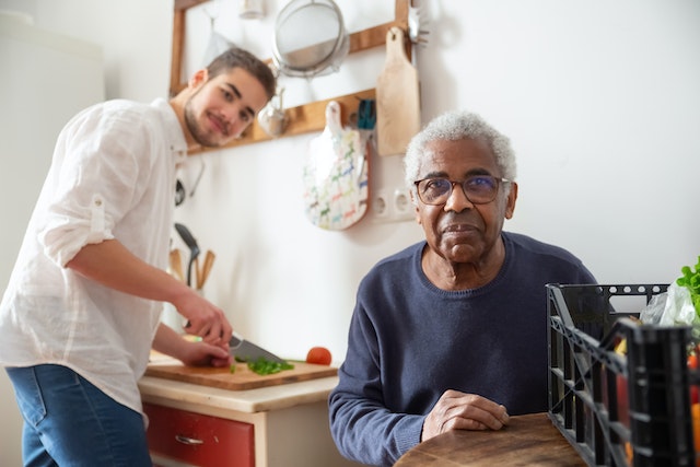 Foto: Ein junger Mann kocht für einen älternen Mann.