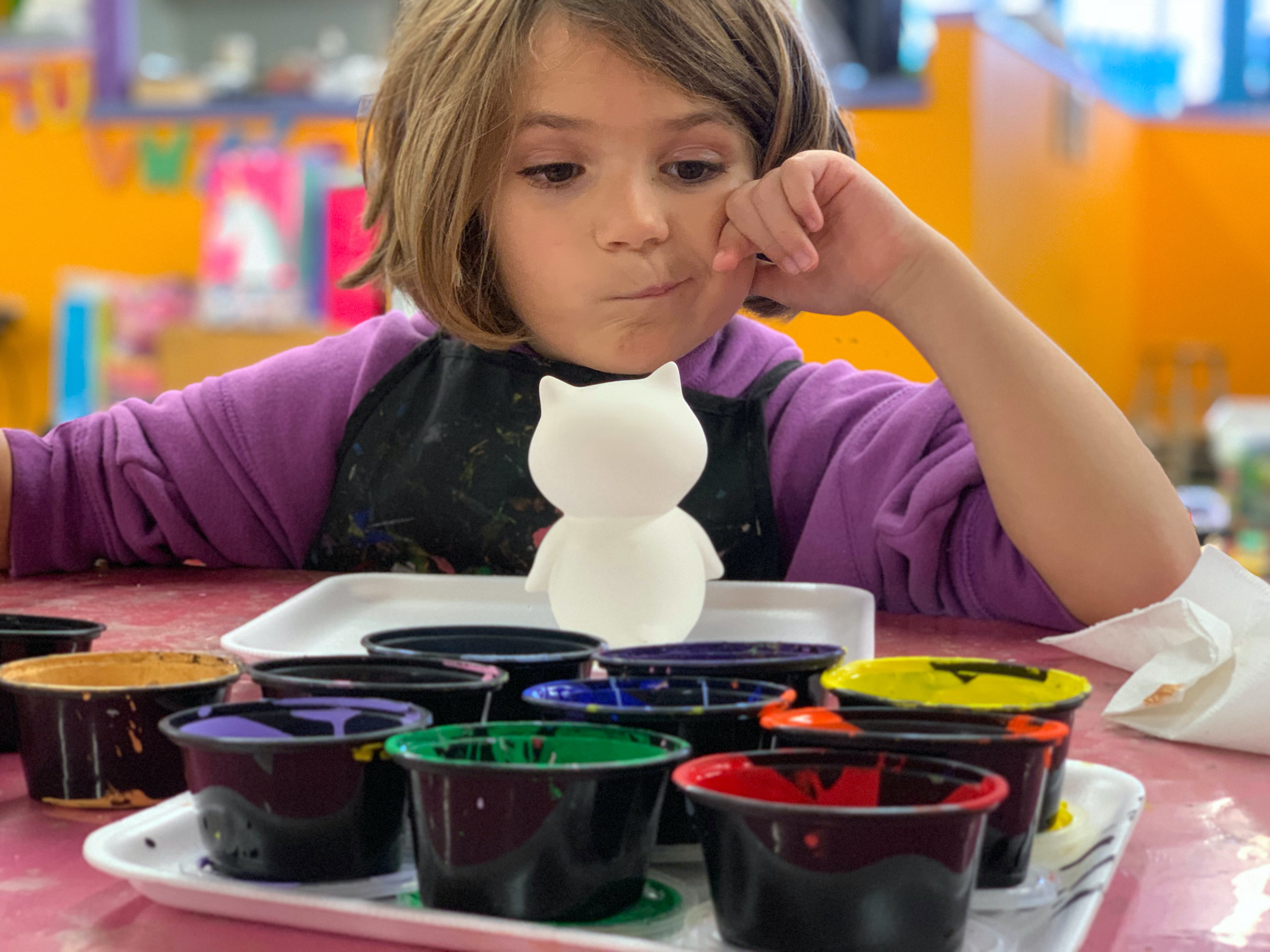 Foto: Ein Kind sitzt vor bunten Farbtöpfen und möchte malen.